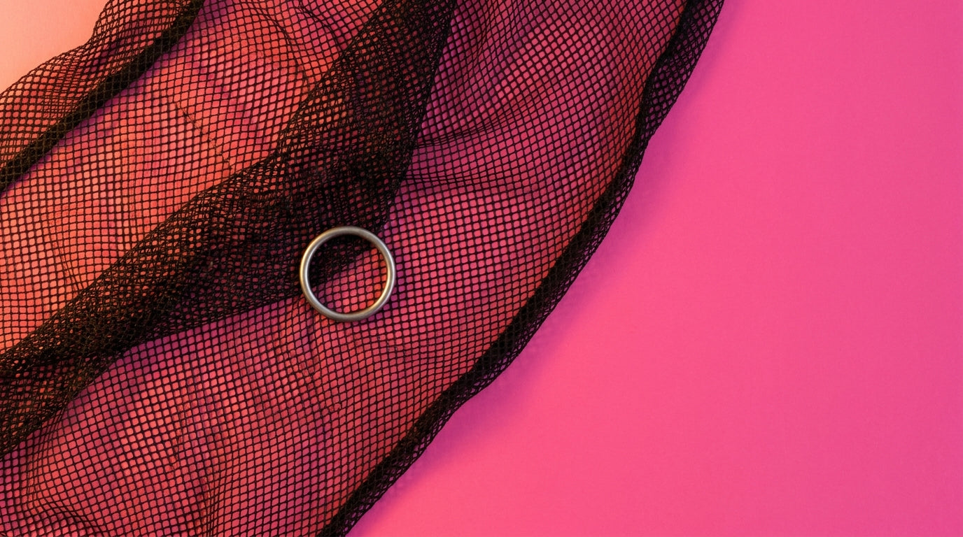 Close-up of black fishnet fabric draped in artful folds with a single silver O-ring resting on top, vivid pink background