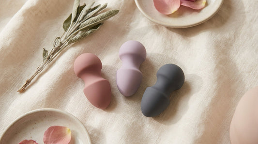A collection of small pastel-coloured silicone butt plugs arranged neatly on a soft cream linen surface