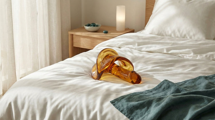 Elegant clear glass pleasure tool on silk bedding with soft lighting