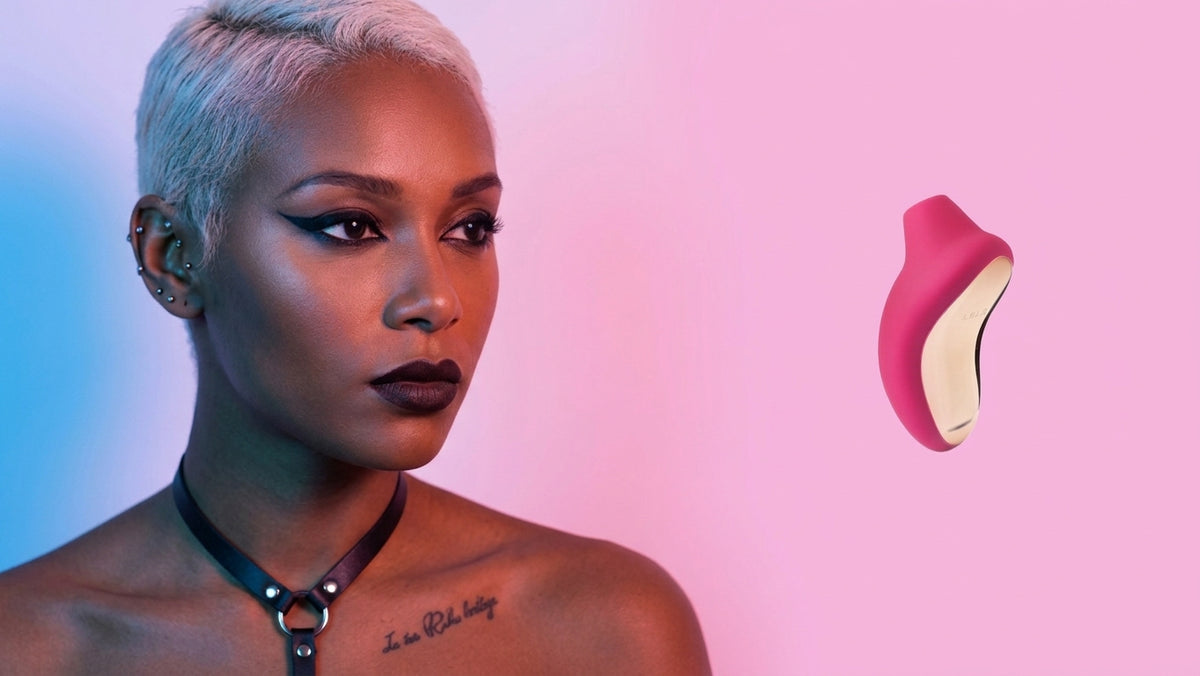 A woman with short platinum blonde hair and a black choker necklace is shown against a pink and blue gradient background, with a floating pink and cream intimate device on the right side.