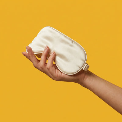 Soft satin blindfold held gently in hand on golden background — bondage and sensory accessories at NaughtyNest UK